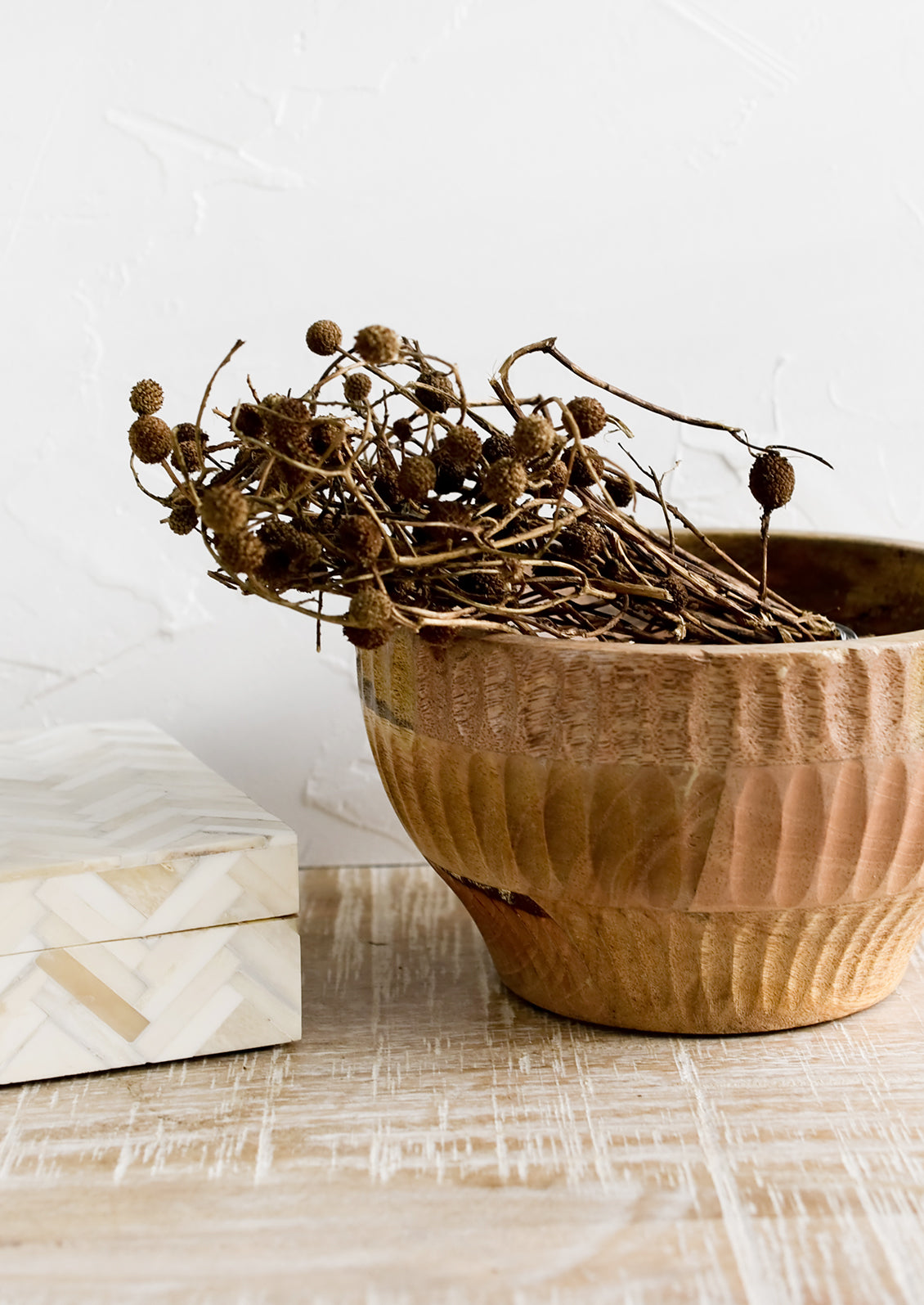 A wooden bowl housing dried seedpod bundle.
