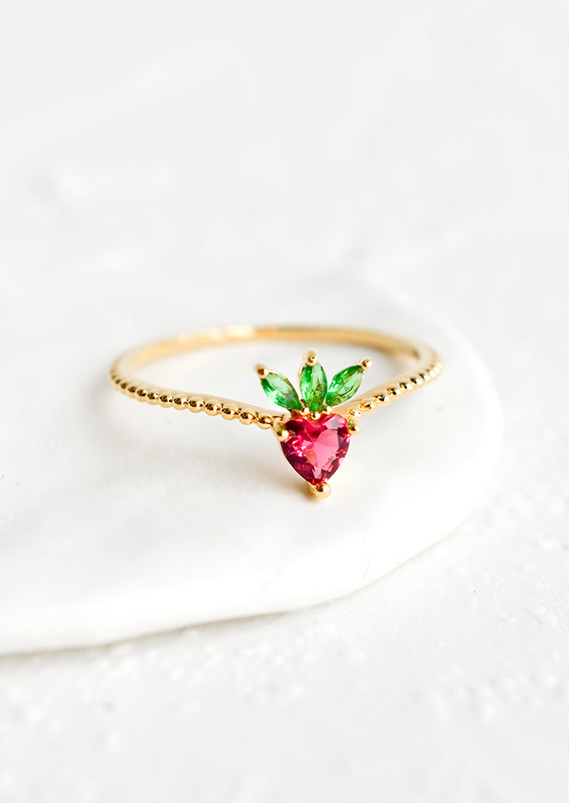 A gold ring with beaded texture and strawberry shaped crystal front.