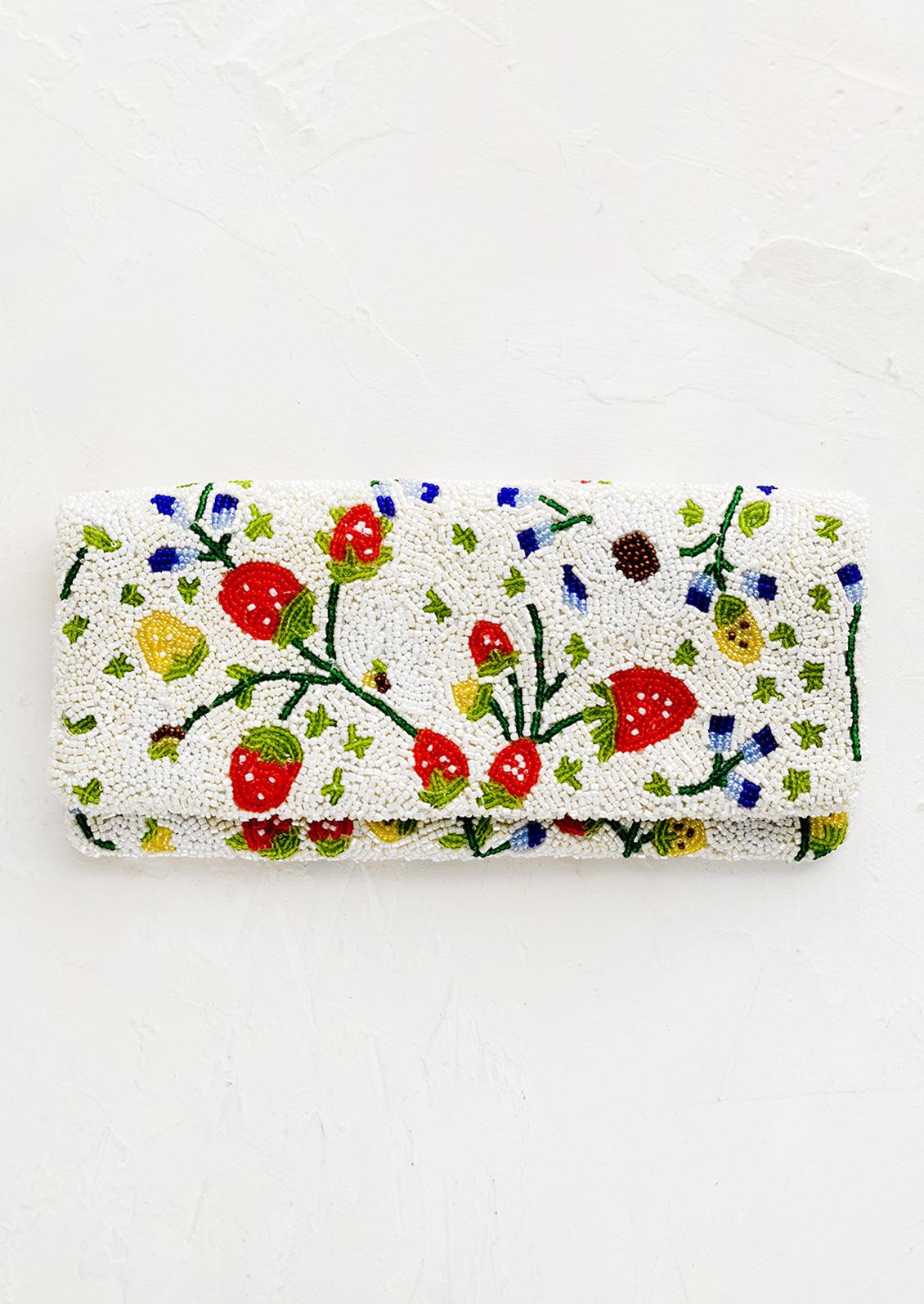 A rectangular foldover beaded clutch in white with multicolor strawberry pattern.