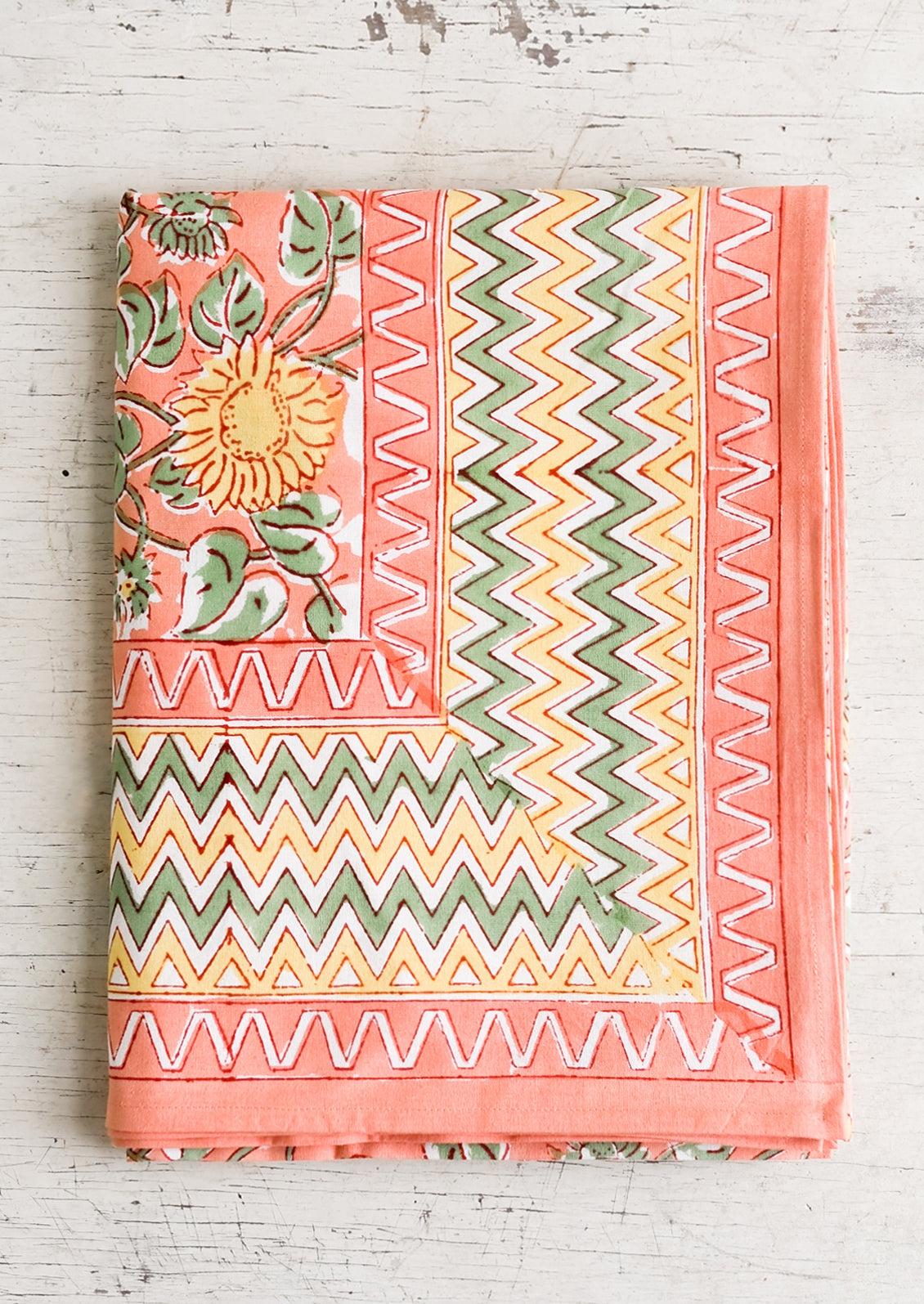 A block printed tablecloth in peach, mint and yellow sunflower pattern with zigzag border.
