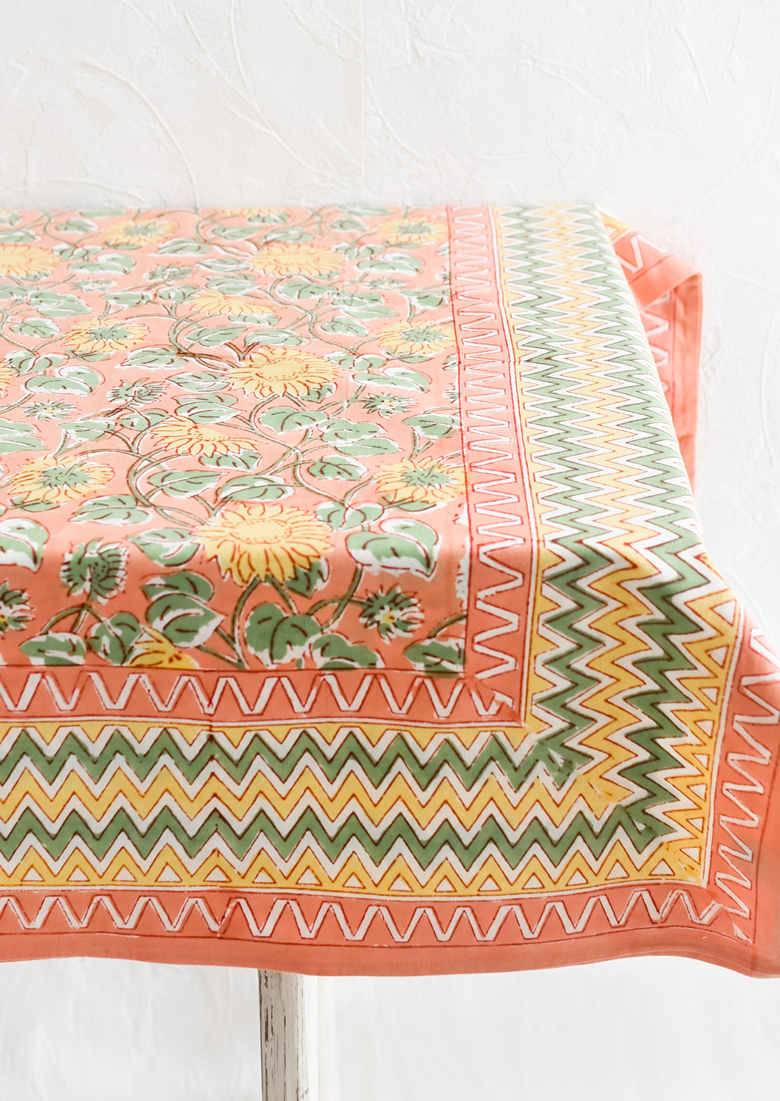 A block printed tablecloth in peach, mint and yellow sunflower pattern with zigzag border.