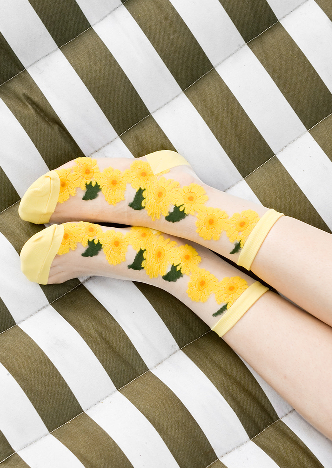 A woman's ankles on a hammock wearing sheer sunflower socks.