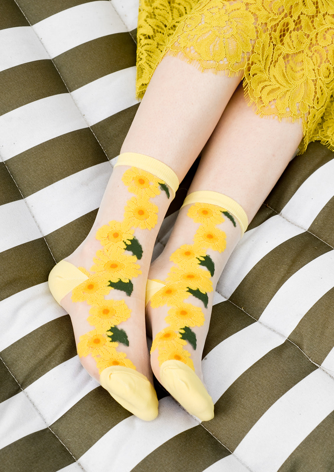 A woman's ankles on a hammock wearing sheer sunflower socks with yellow lace skirt.