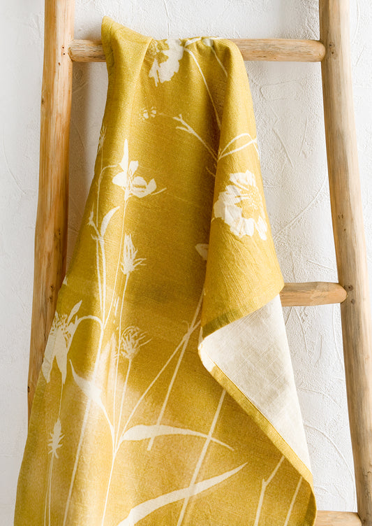 A yellow cotton tea towel with "bleached" look floral print.