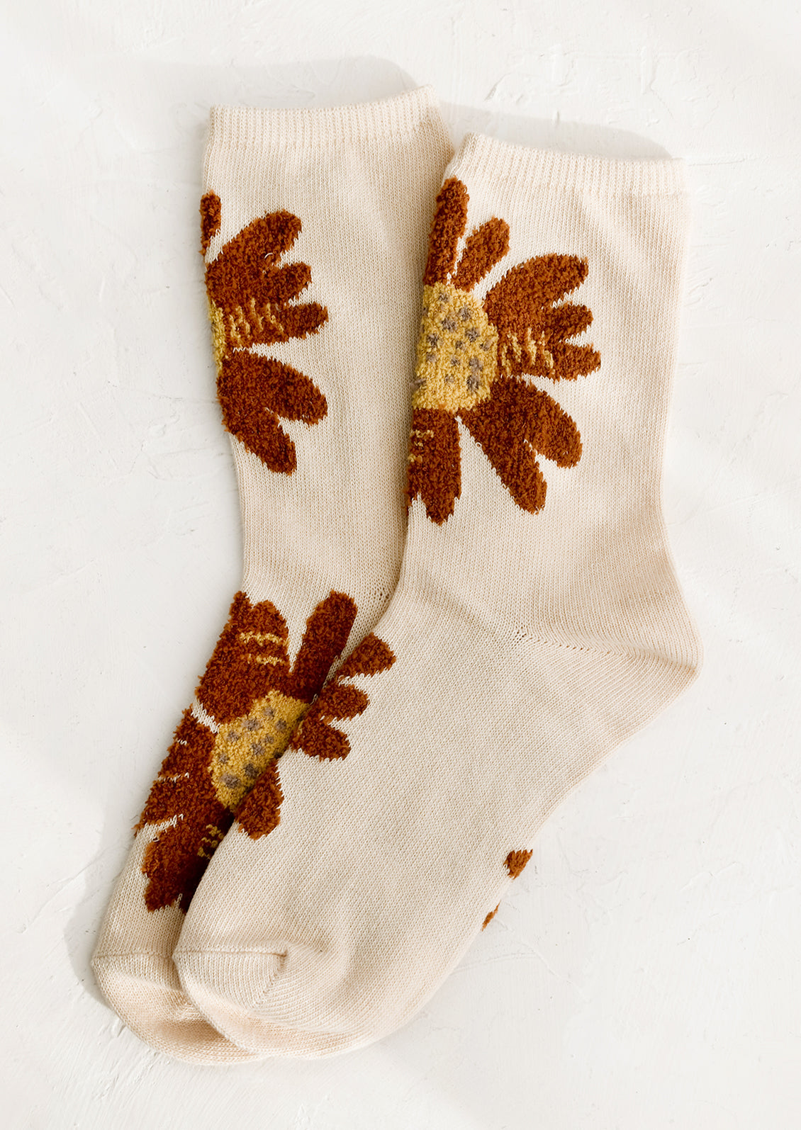 A pair of cream colored socks with fuzz textured, rust-colored flowers.