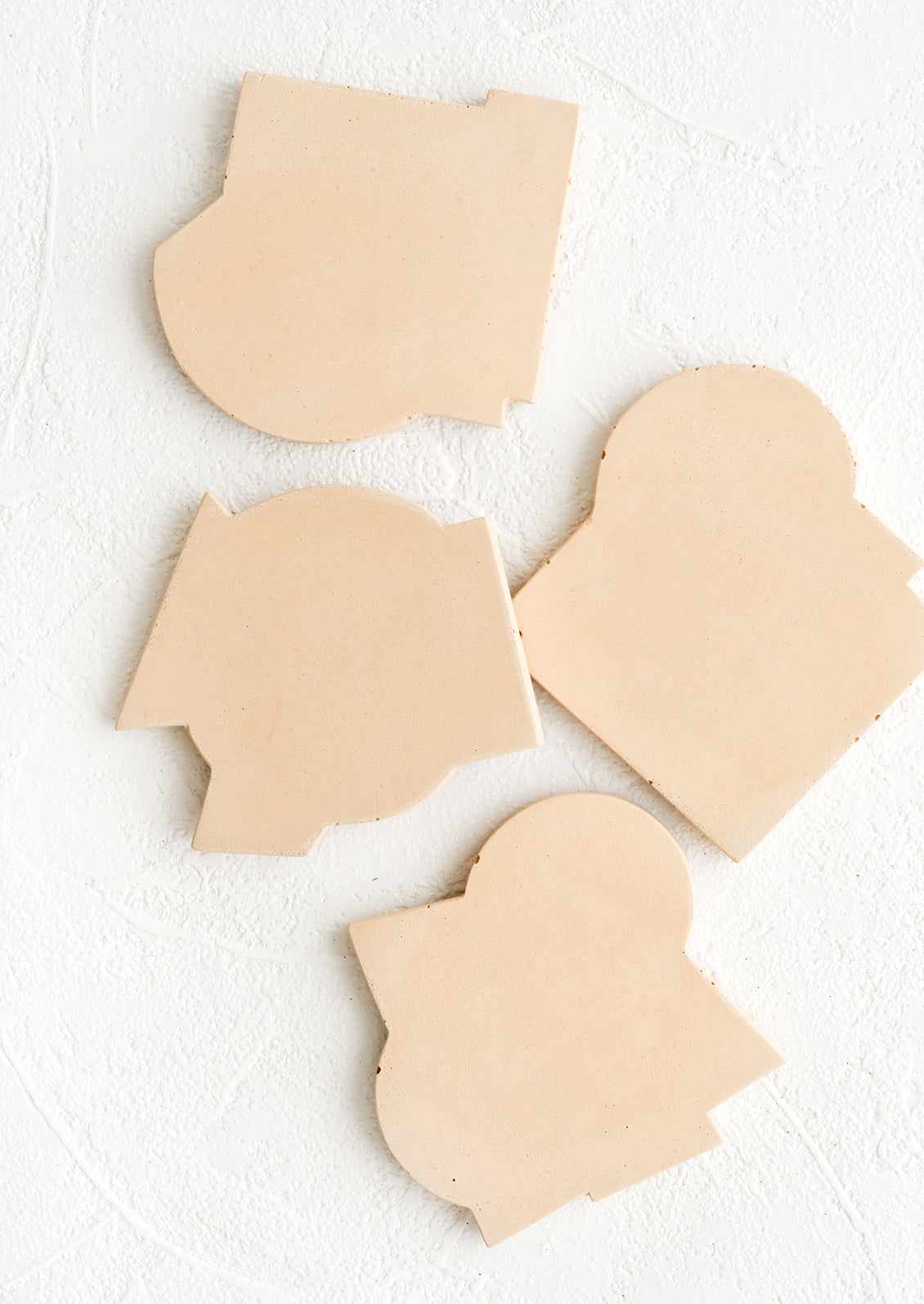 Four concrete coasters in nude color with unique abstract shapes.