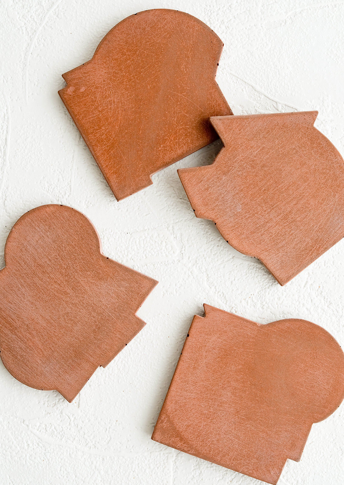 Four concrete coasters in rust color with unique abstract shapes.