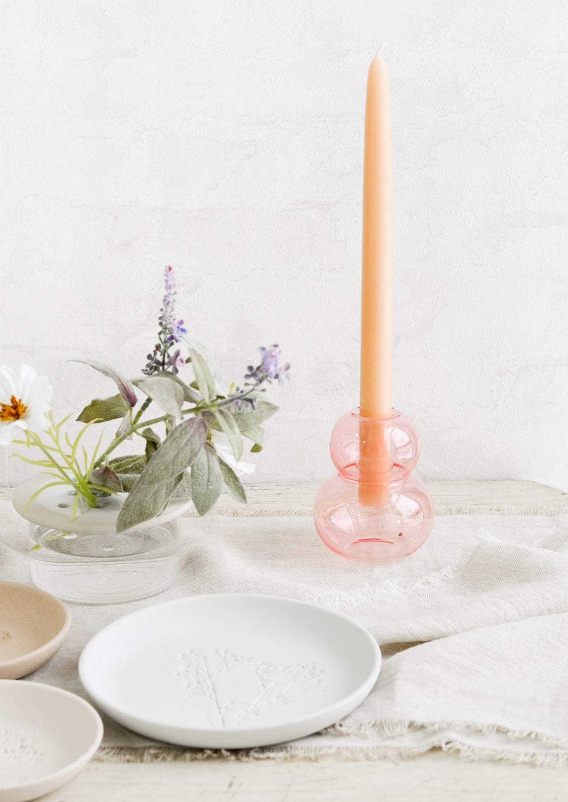 A tablescape scene featuring ceramic plates and a pink glass taper candle holder.