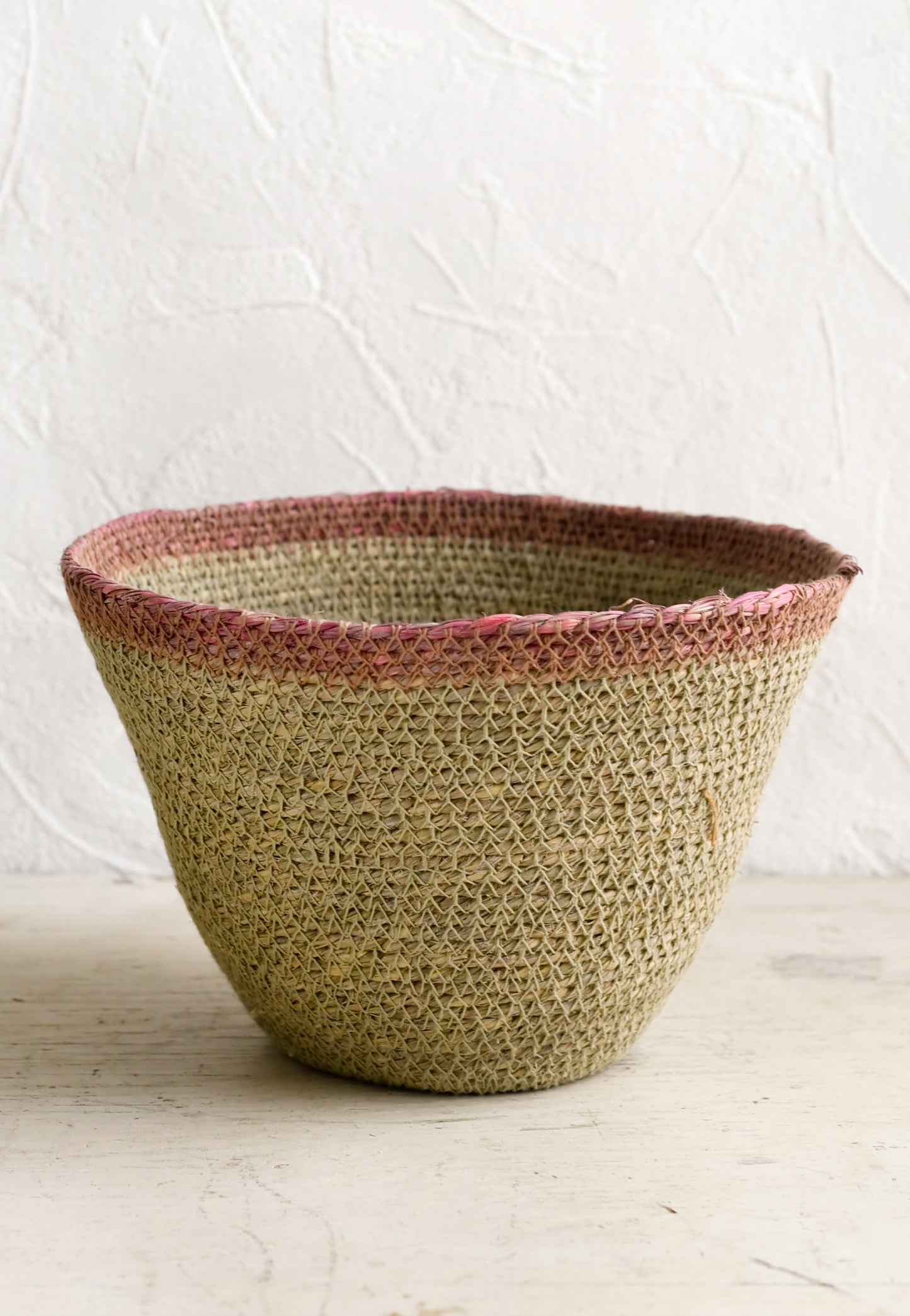 A tapered seagrass storage basket in natural with pink rim.