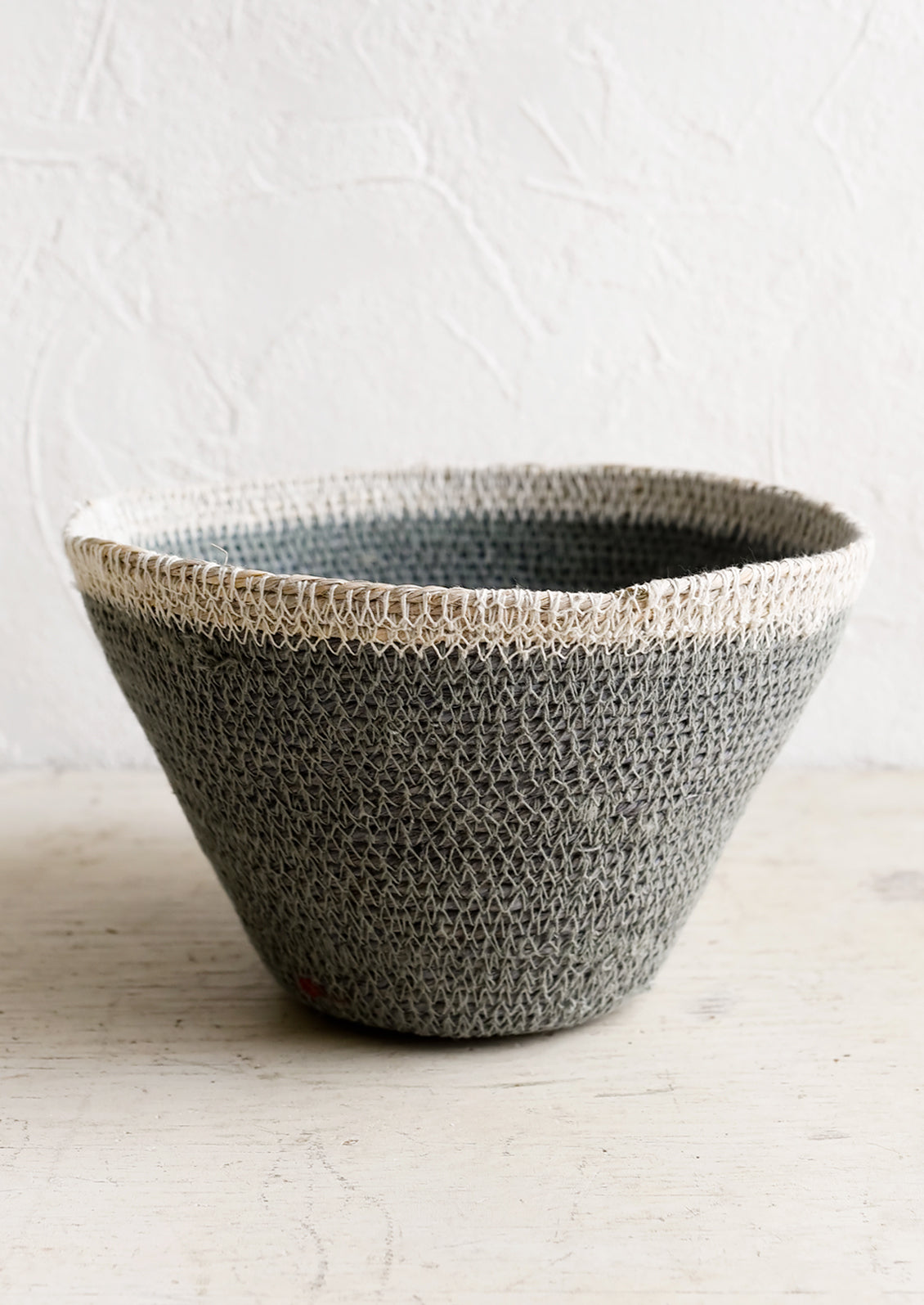 A tapered seagrass storage basket in dusty blue with white rim.
