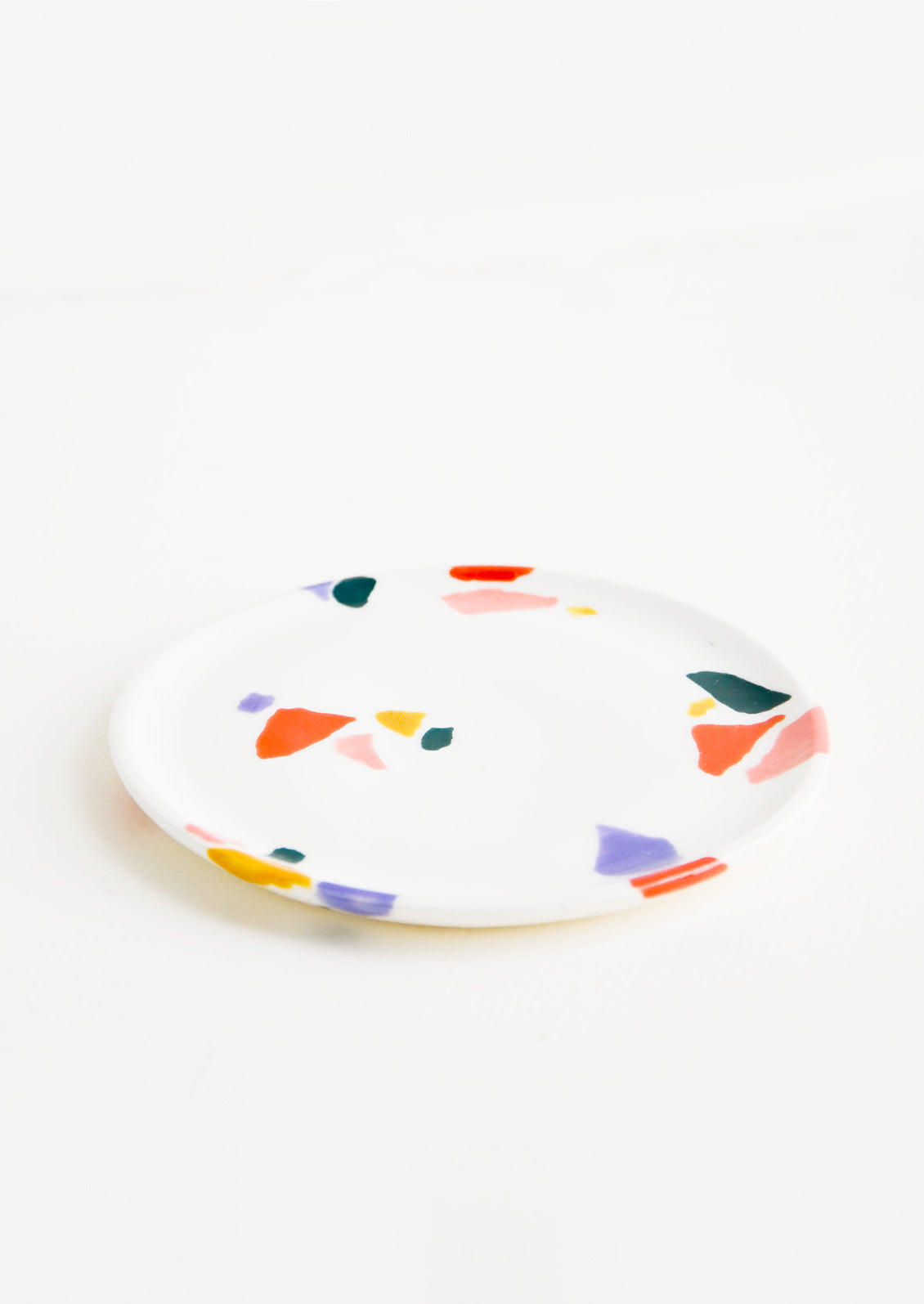 Small, plate-like ceramic dish in ivory with hand-painted, fragmented pattern in a mix of colors