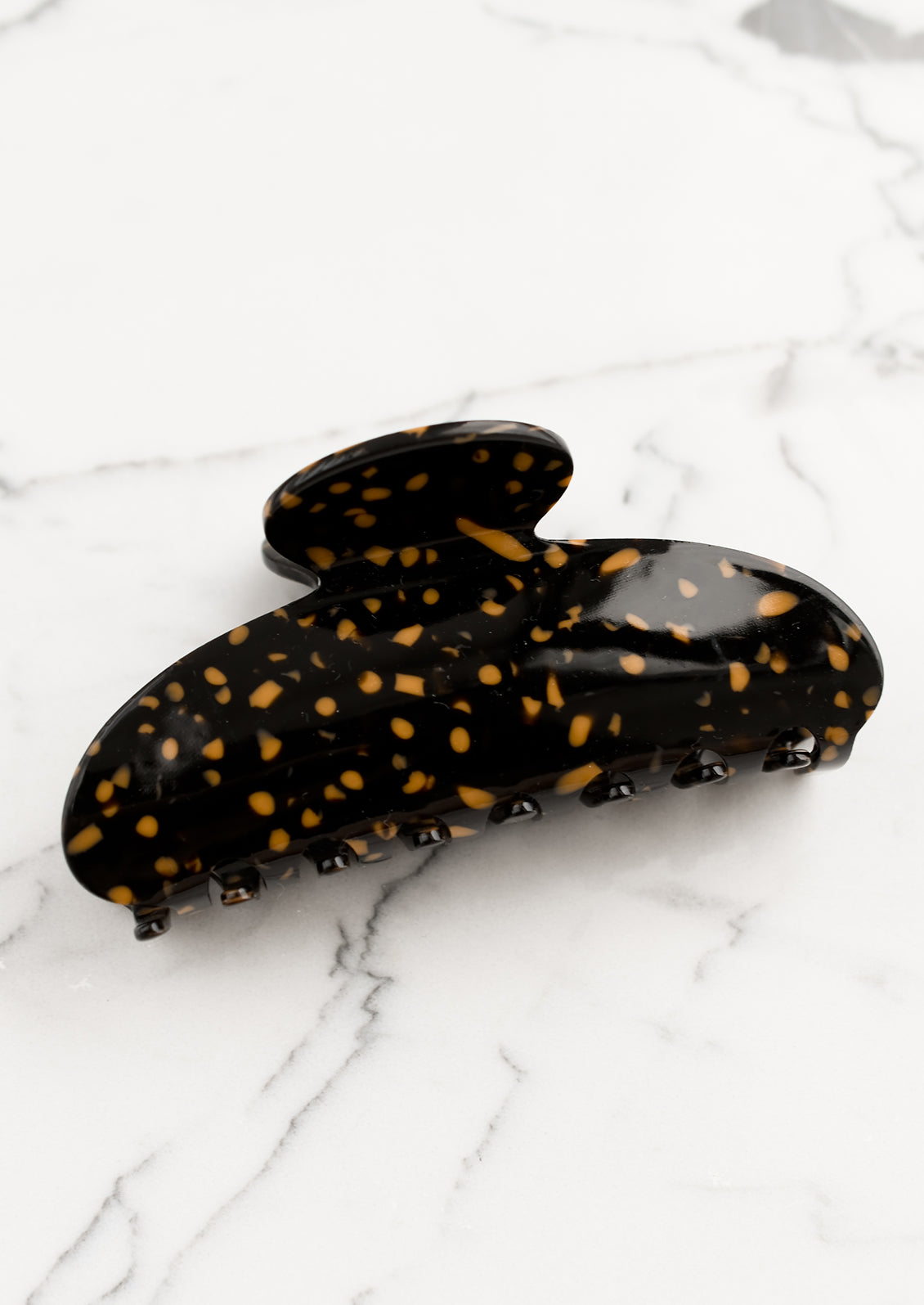 A terrazzo hair claw in black with toffee spots.