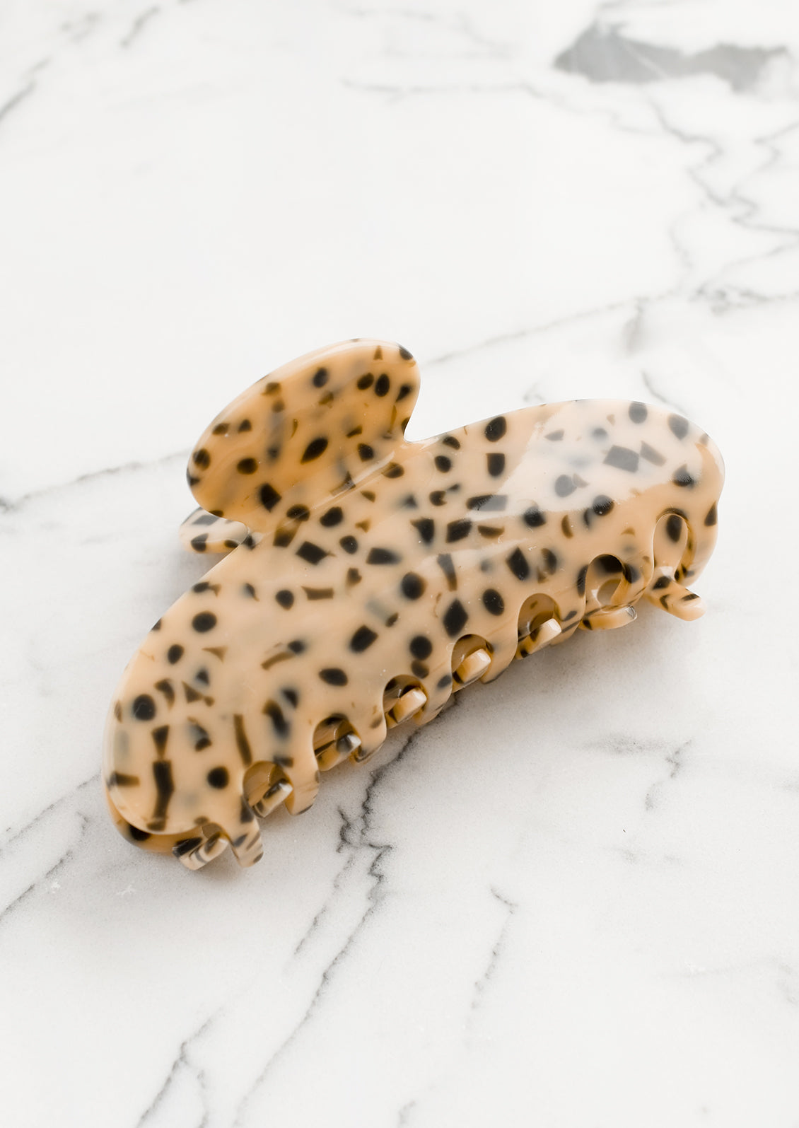 A terrazzo hair claw in chai with grey spots.