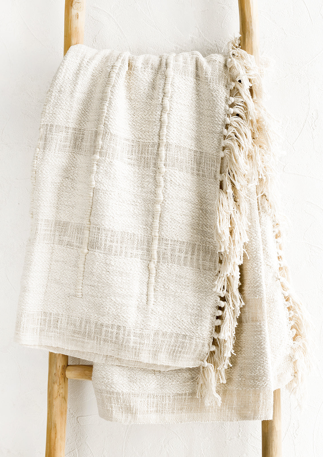 A natural cotton throw with paneling detailing and fringed trim.