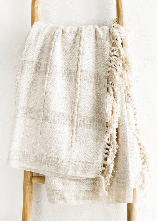 A natural cotton throw with paneling detailing and fringed trim.