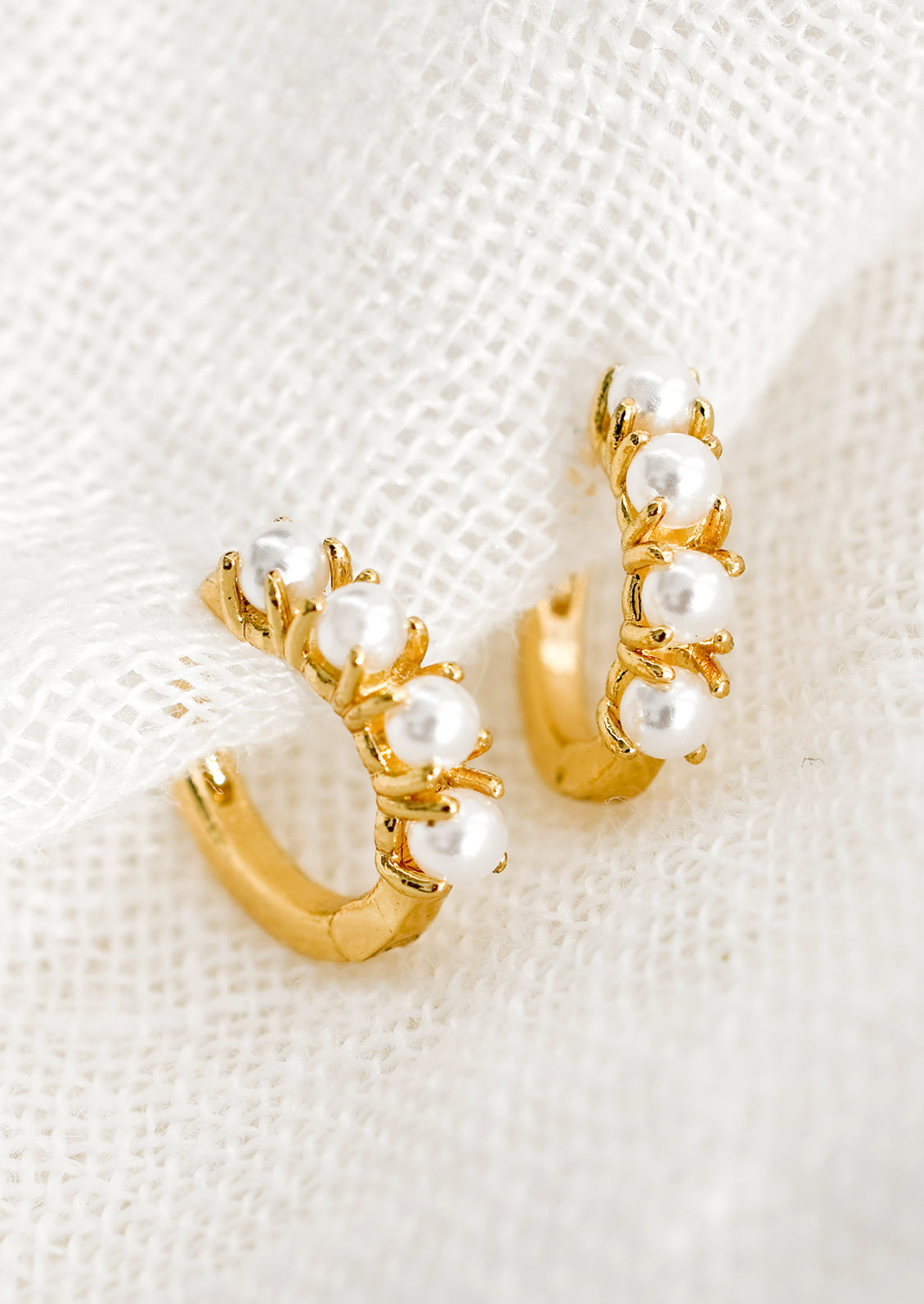 A pair of small gold huggie hoop earrings with round pearl detailing.