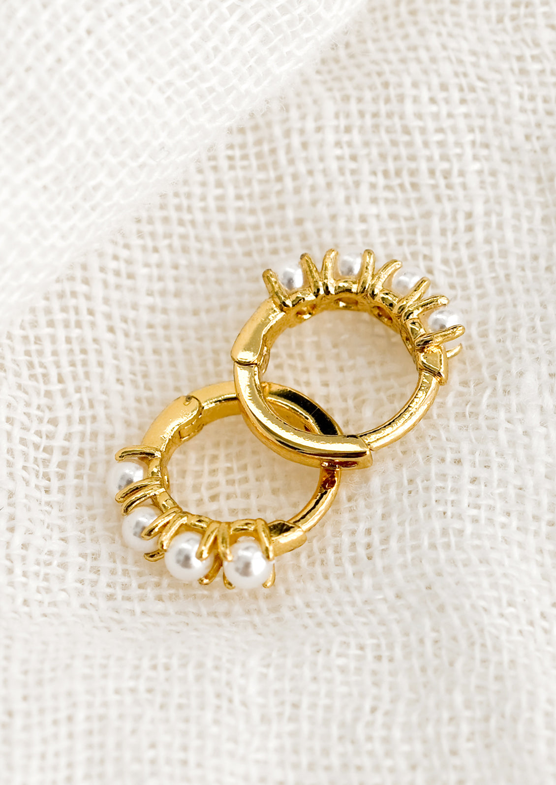 A pair of small gold huggie hoop earrings with round pearl detailing.