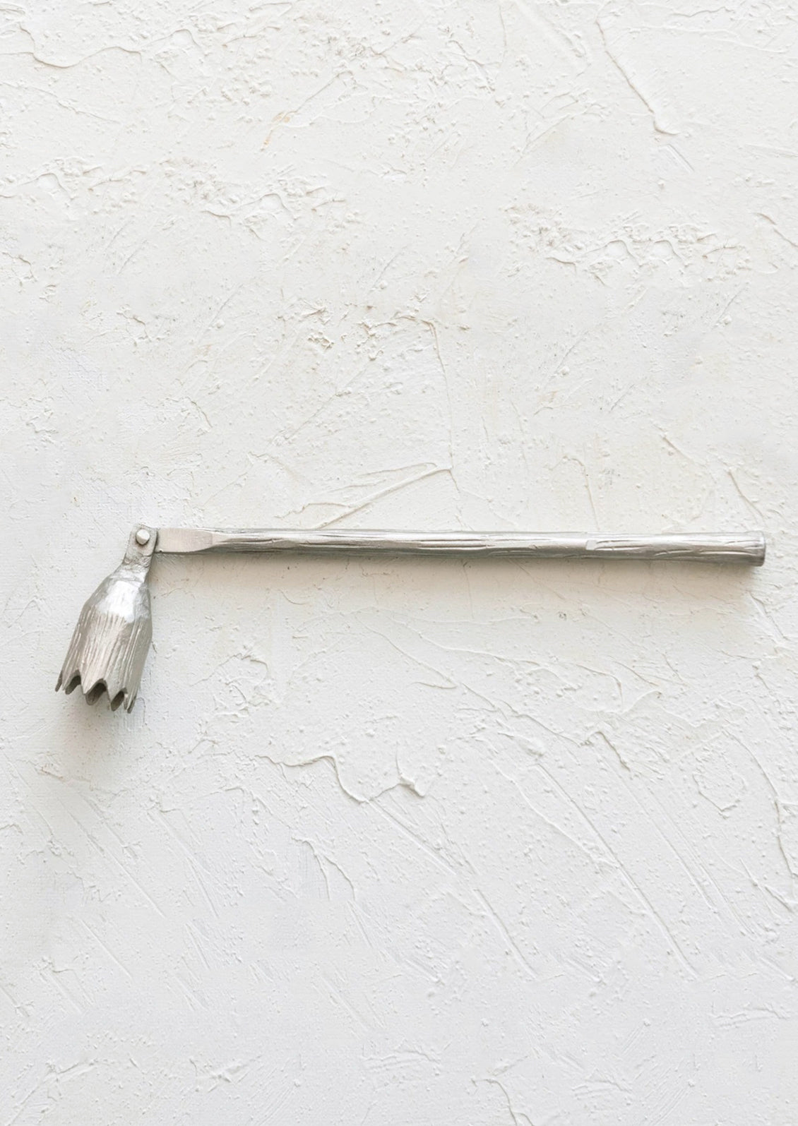 A pewter metal candle snuffer with abstract flower shape.