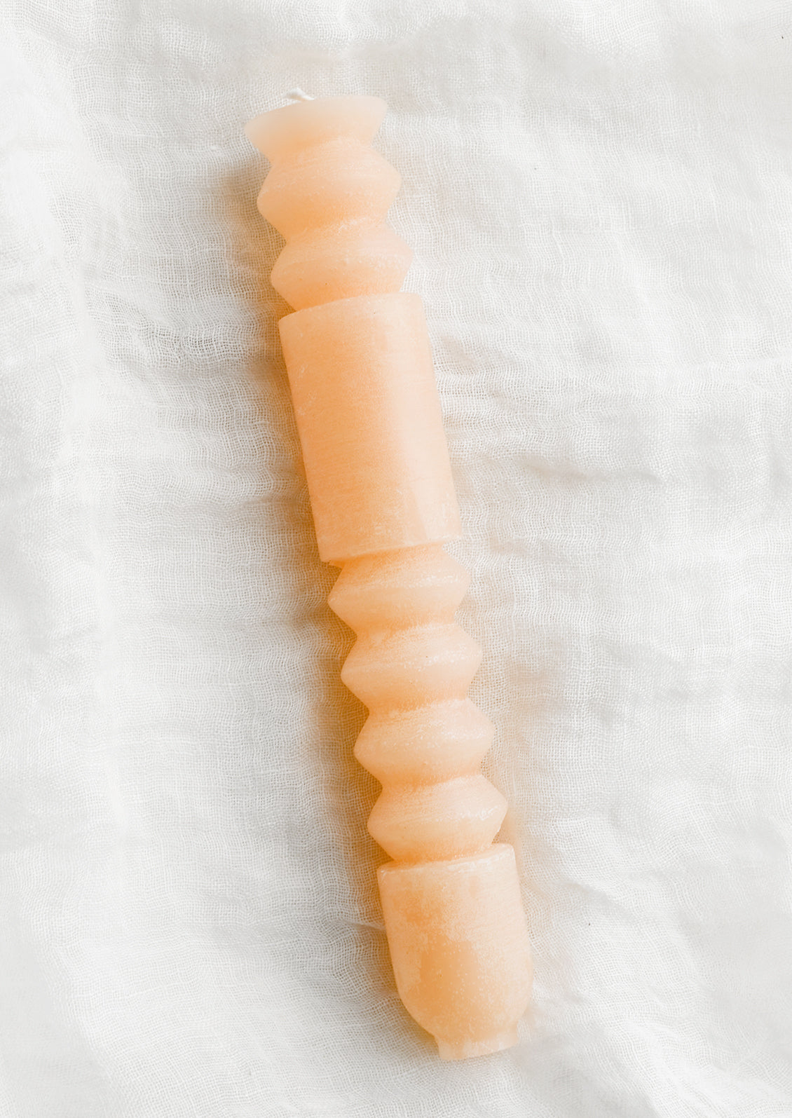 A geometric shape taper candle in pomelo (peach).