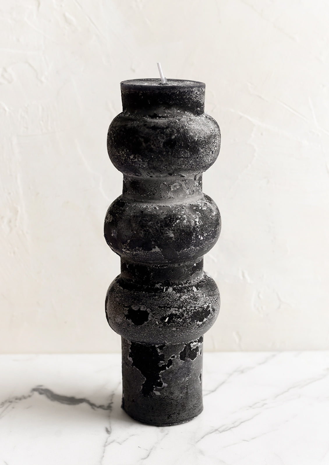 A large hourglass shaped pillar candle with waxy finish in black.