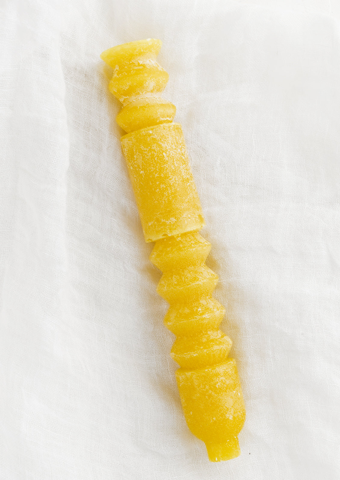 A geometric shape taper candle in beeswax (yellow).
