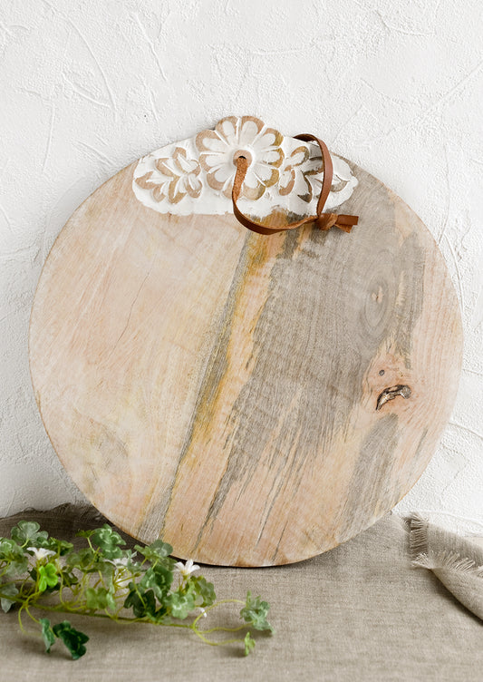 A round wooden cutting board with shabby chic floral detailing.