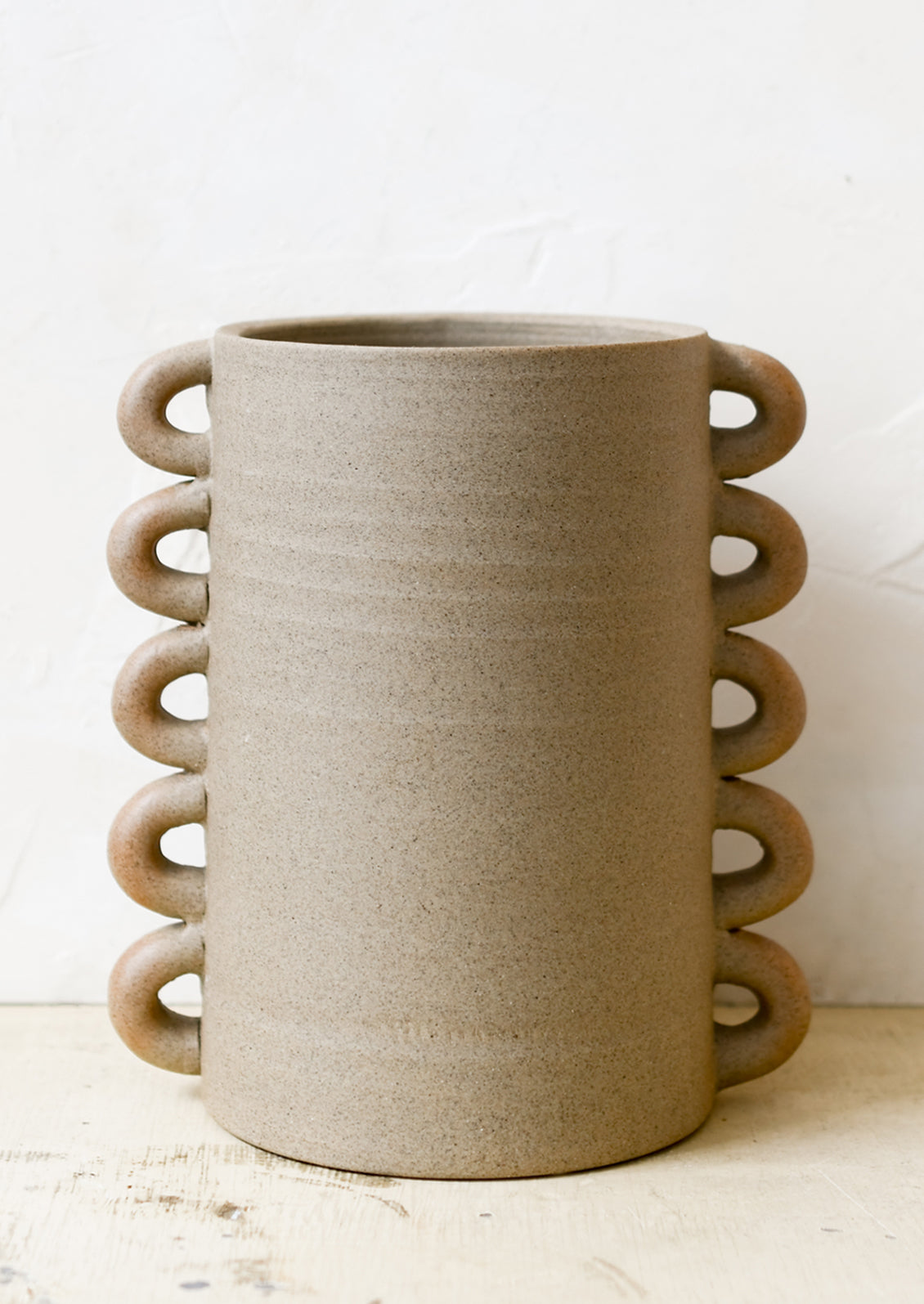 A raw sand clay vase with decorative loops all the way down both sizes.