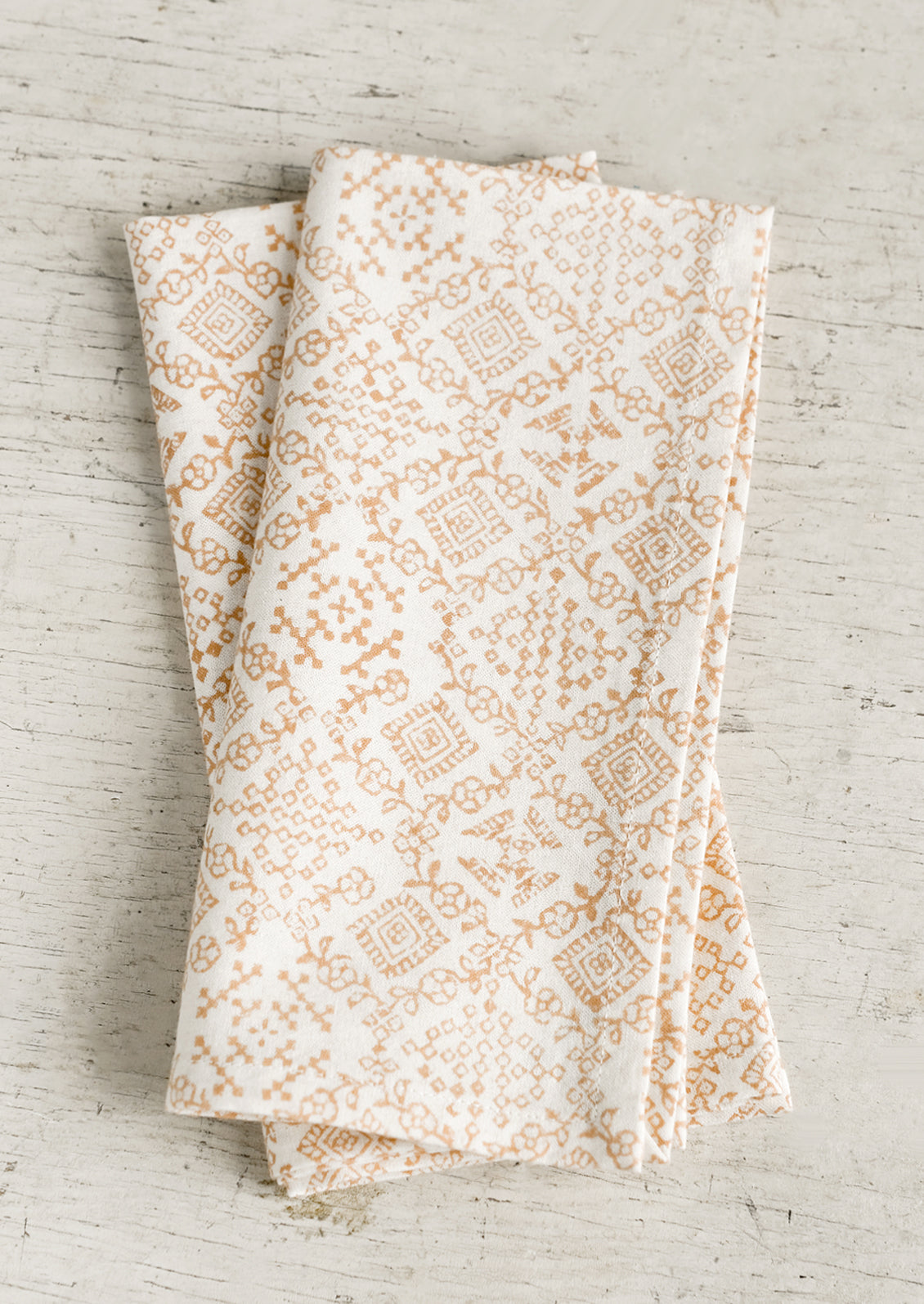 A pair of cream napkins with peach tile print.