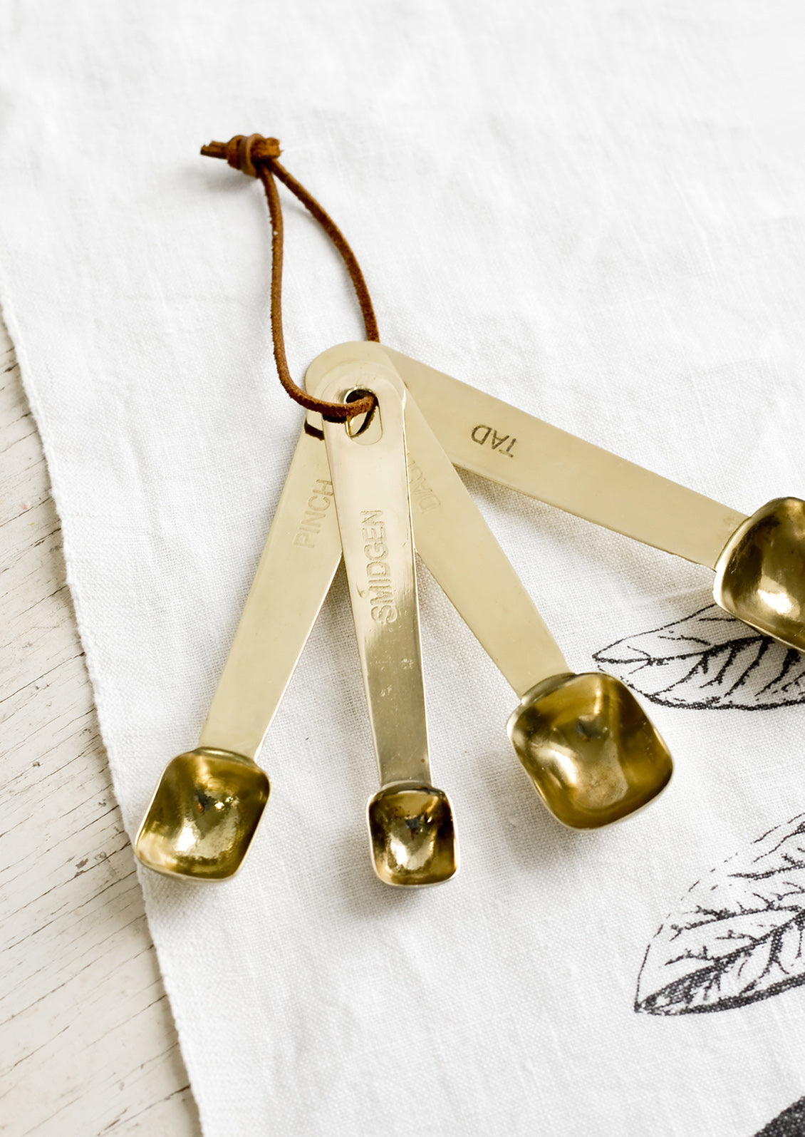 A set of four golden measuring spoons with brown leather tie.