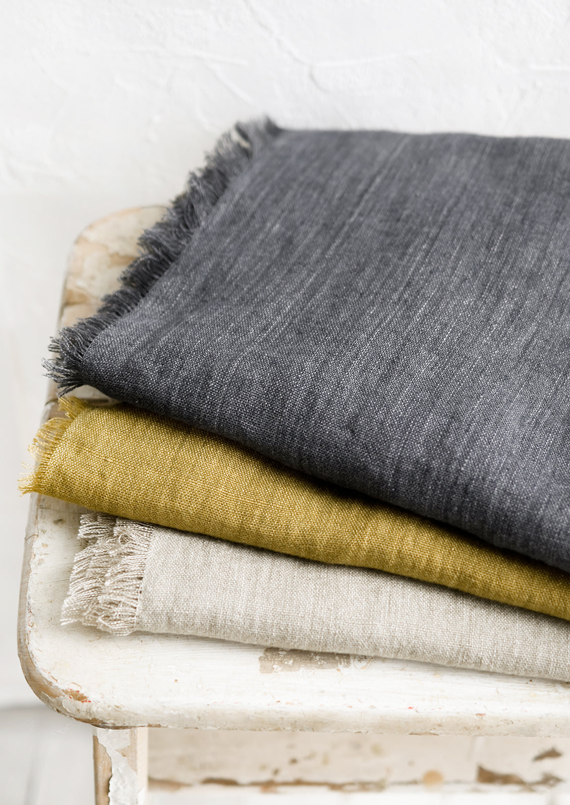 A stack of frayed edge linen table runners in three different colors.