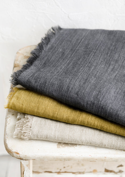 A stack of frayed edge linen table runners in three different colors.