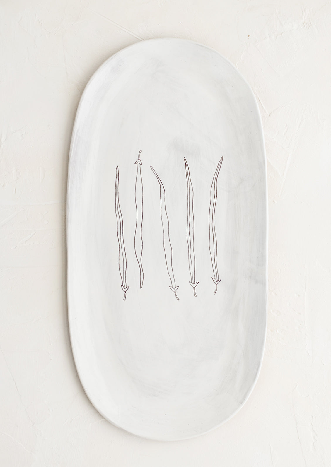 An oval shaped ceramic serving platter with hand drawn green beans illustration at center.