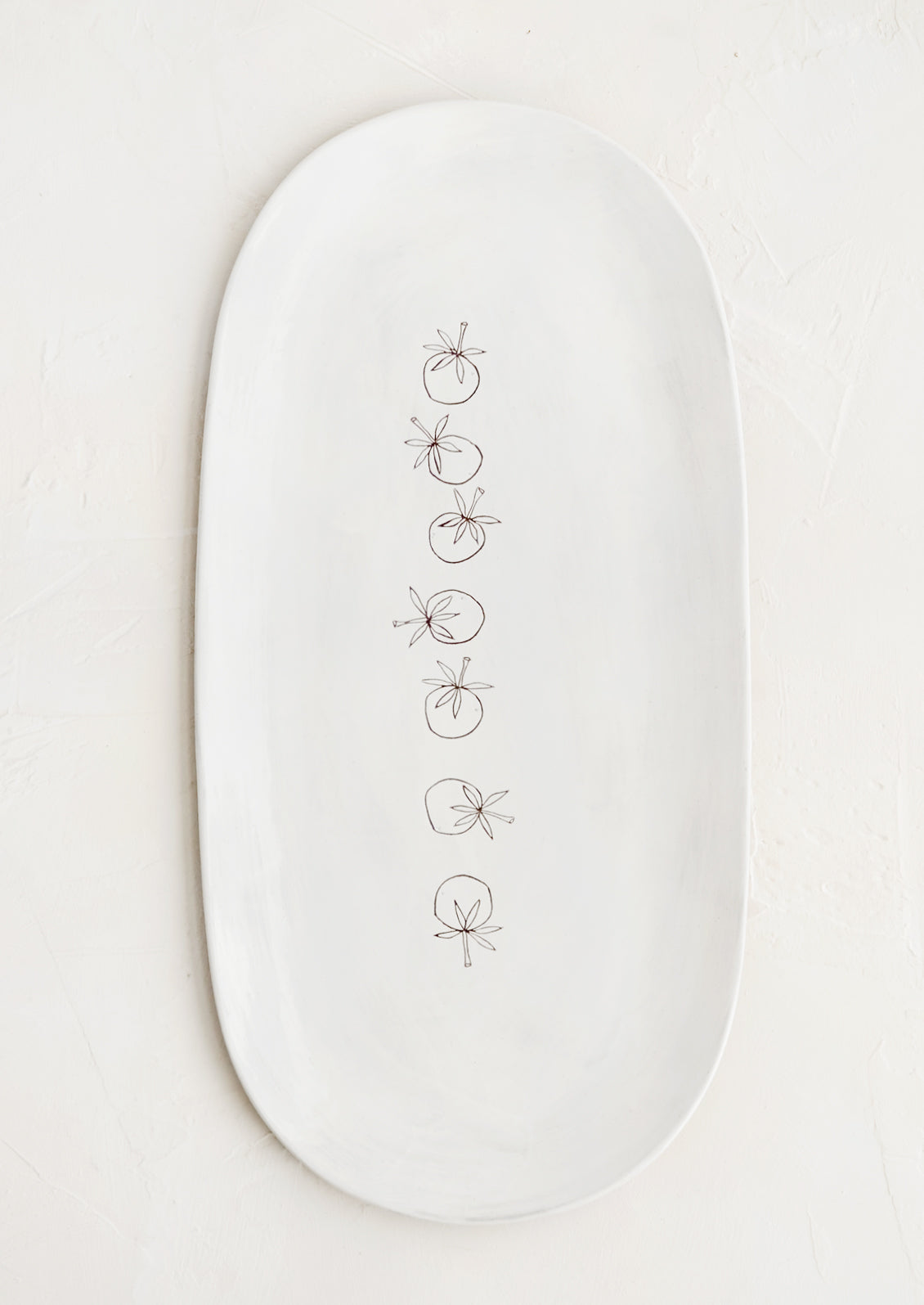 An oval shaped ceramic serving platter with hand drawn tomatoes illustration at center.