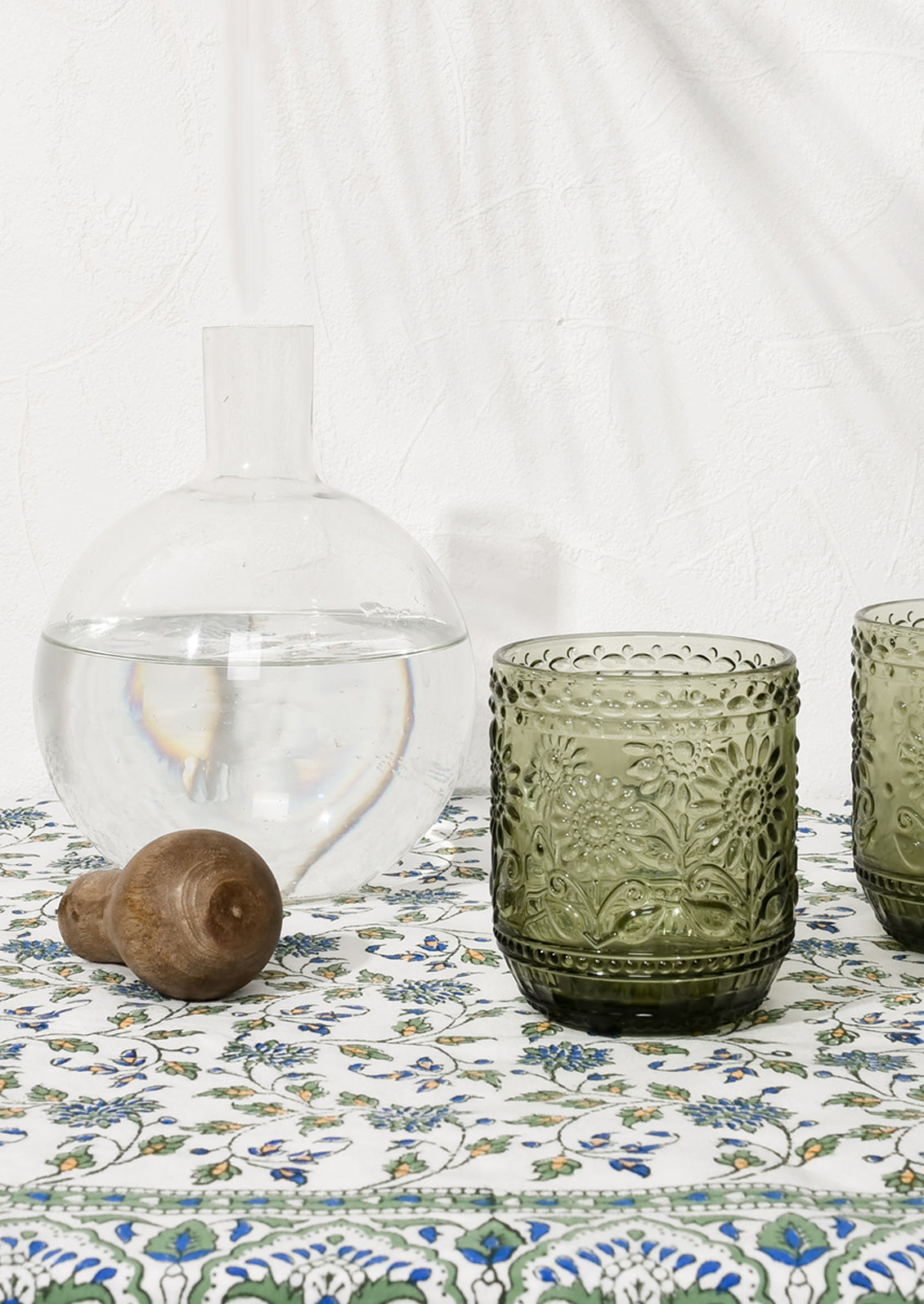 Olive green glasses pictured with a decanter holding water.