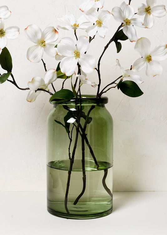 A tall green glass vase with dogwood branches.