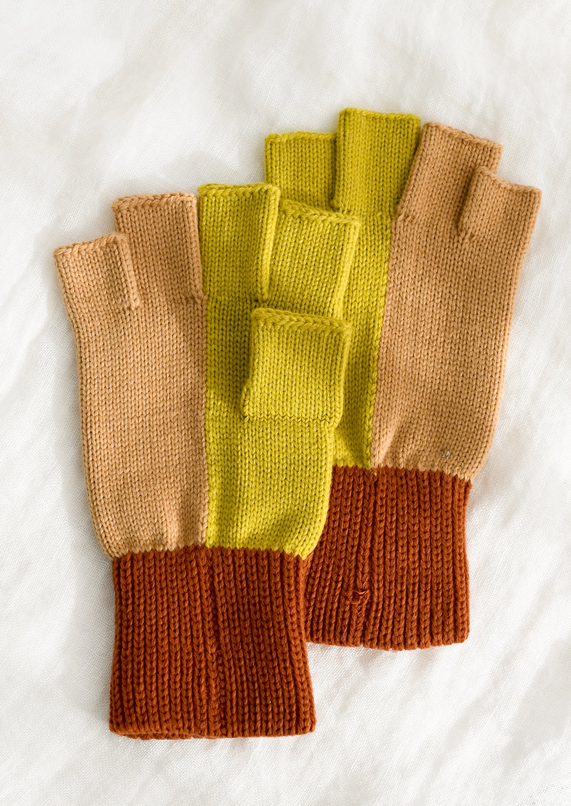 A pair of knit fingerless gloves in terracotta, peach and citrine colorblock.