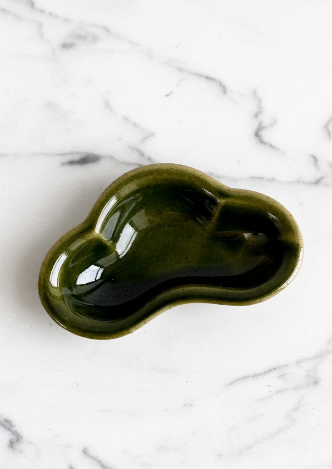 A small ceramic dish in cloud shape and glossy olive green glaze.