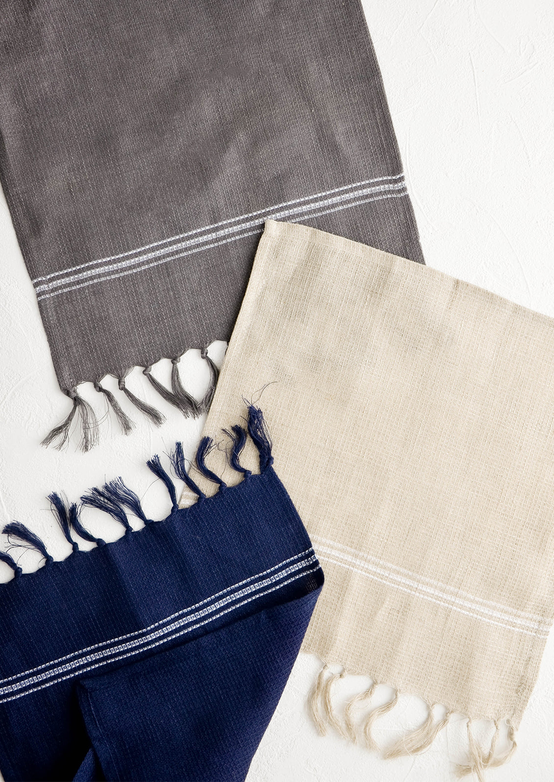 Waffle-textured dishcloths in classic neutral colors with single white stripe detail and tassel trim