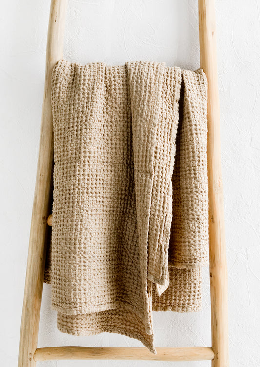 A waffled throw in beige folded over a display ladder.