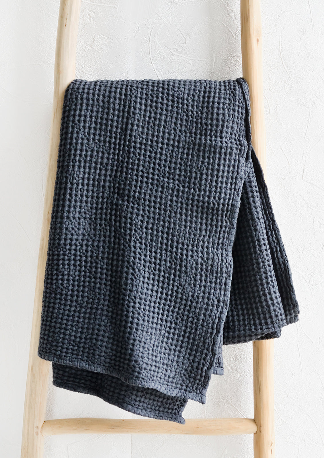 A waffled throw in charcoal folded over a display ladder.