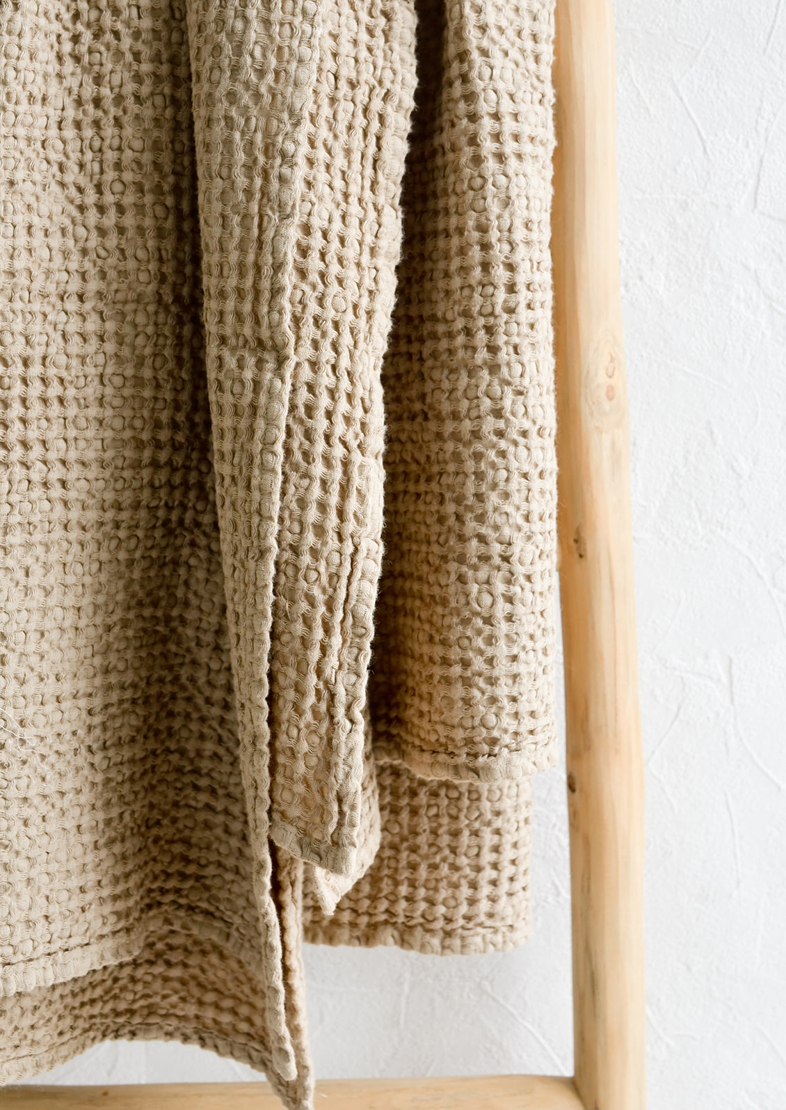 A waffled throw in beige folded over a display ladder.