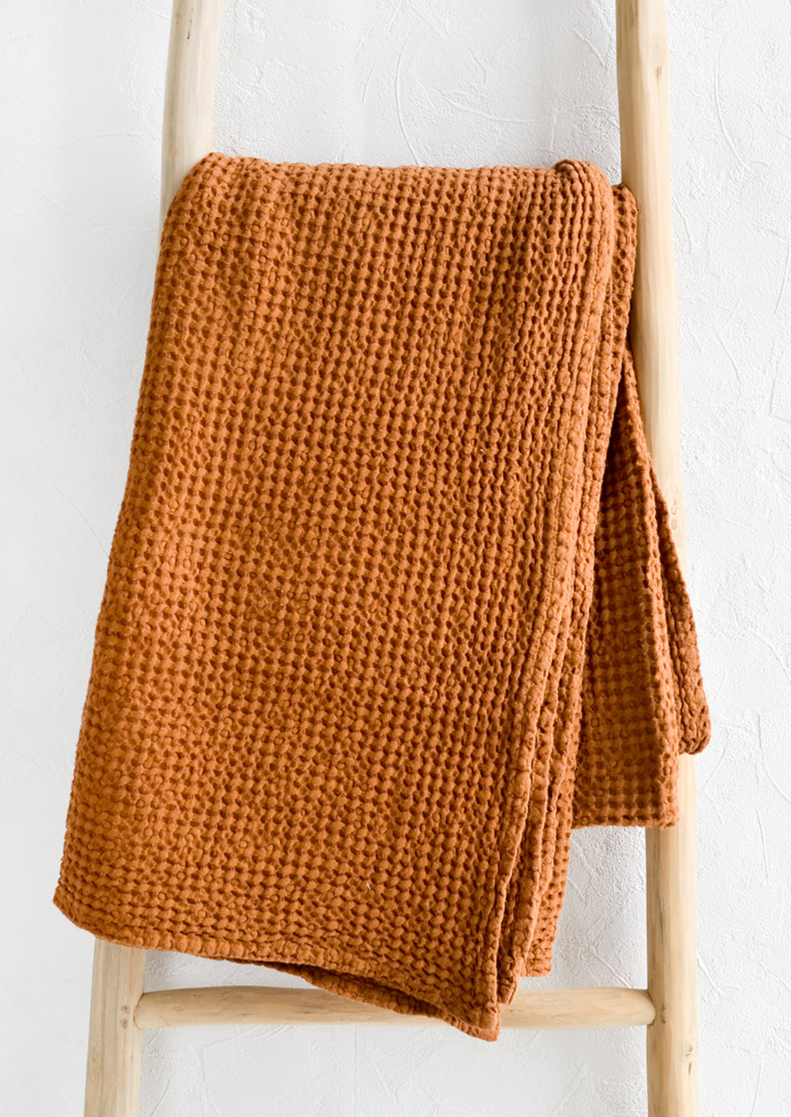 A waffled throw in whiskey folded over a display ladder.