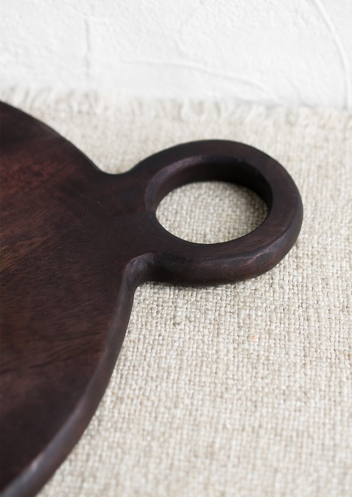 A dark wash wood cutting board with circular shape and cutout circle handle.