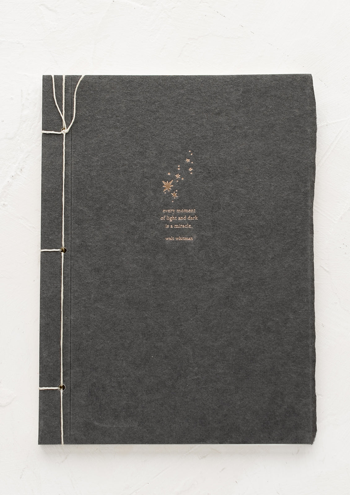 A journal with dark grey cover with Walt Whitman quote.