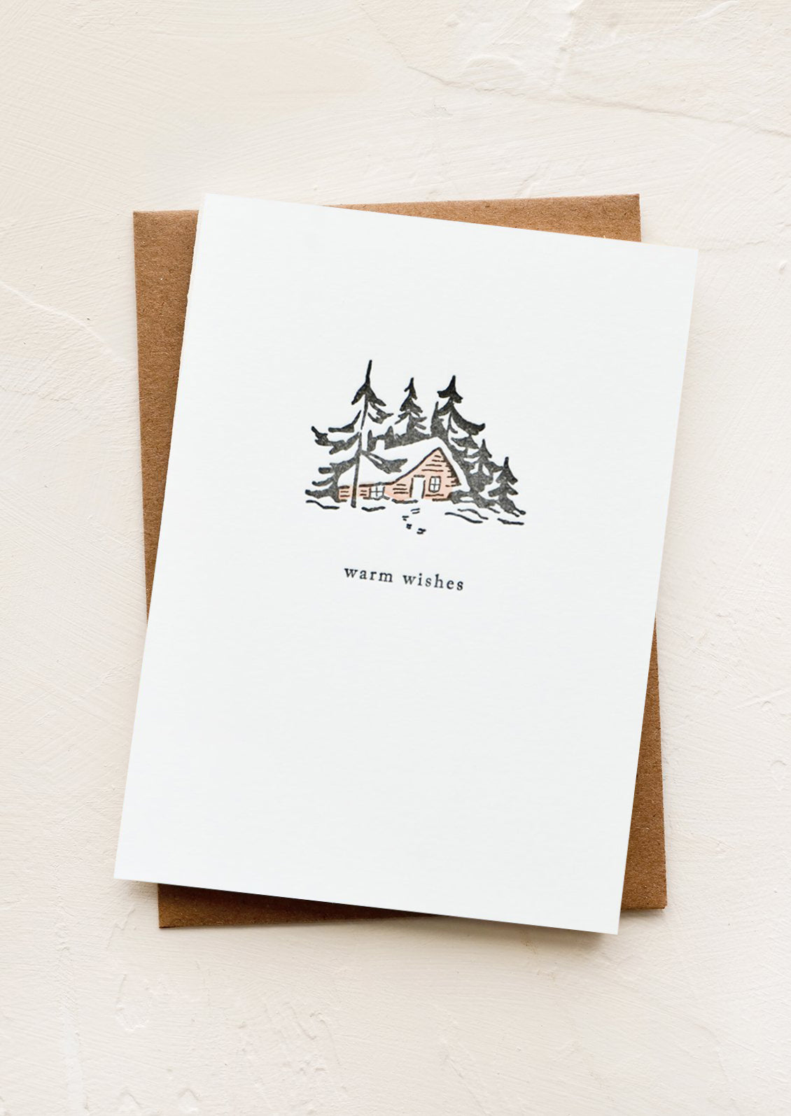 A letterpress printed greeting card with an image of a cabin in the words, text below image reads "warm wishes"