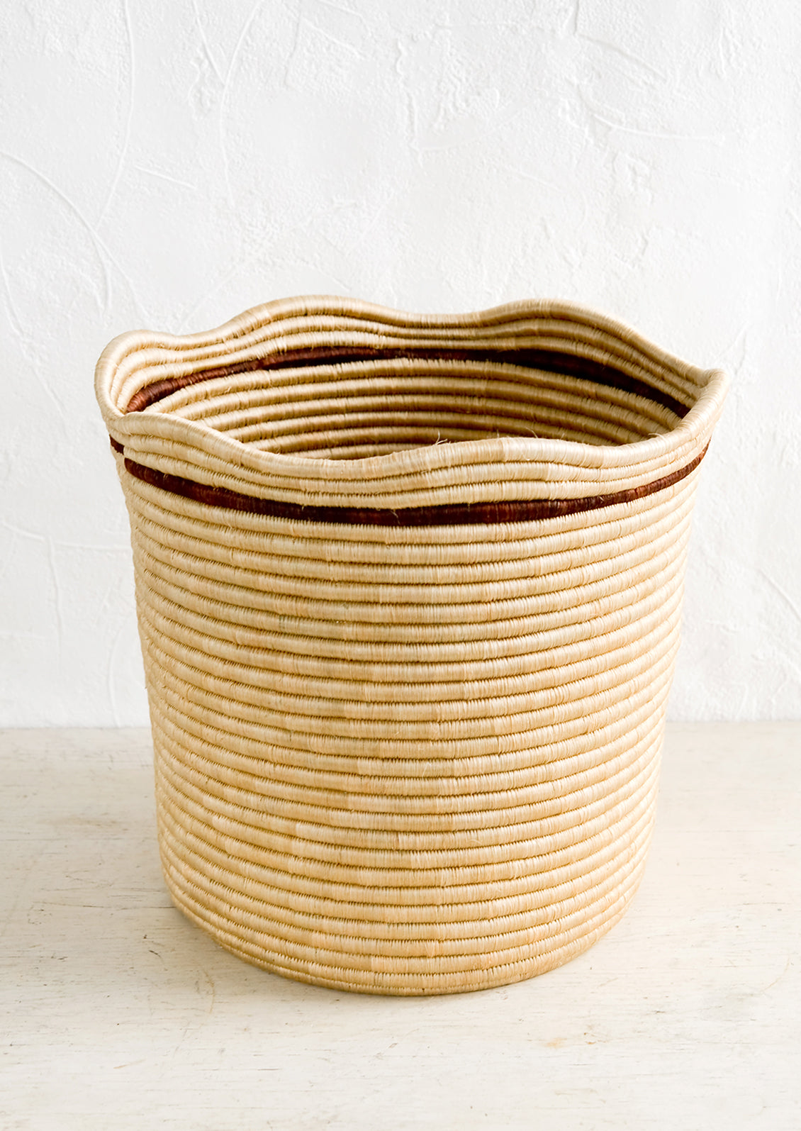 A woven sweetgrass storage bin in natural color with a wavy top rim and contrast stripe detail around rim.
