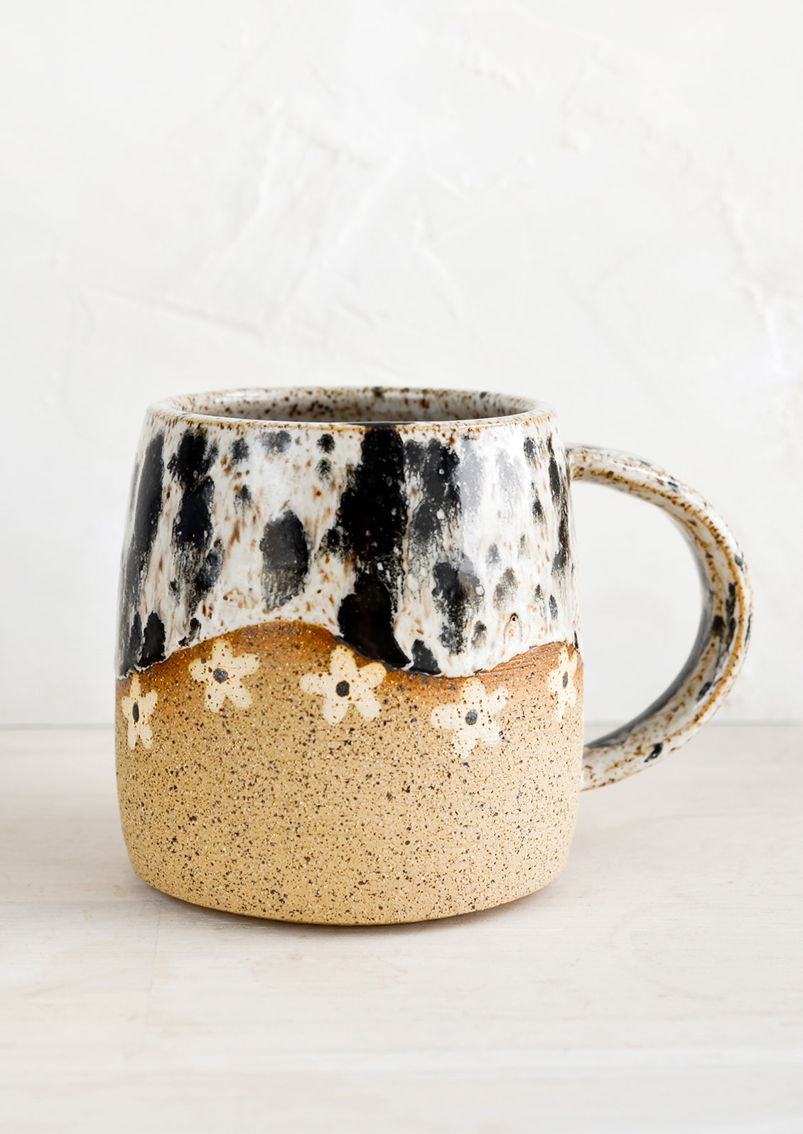 A speckled ceramic coffee mug in black and white with wavy line of ivory daisies at middle.