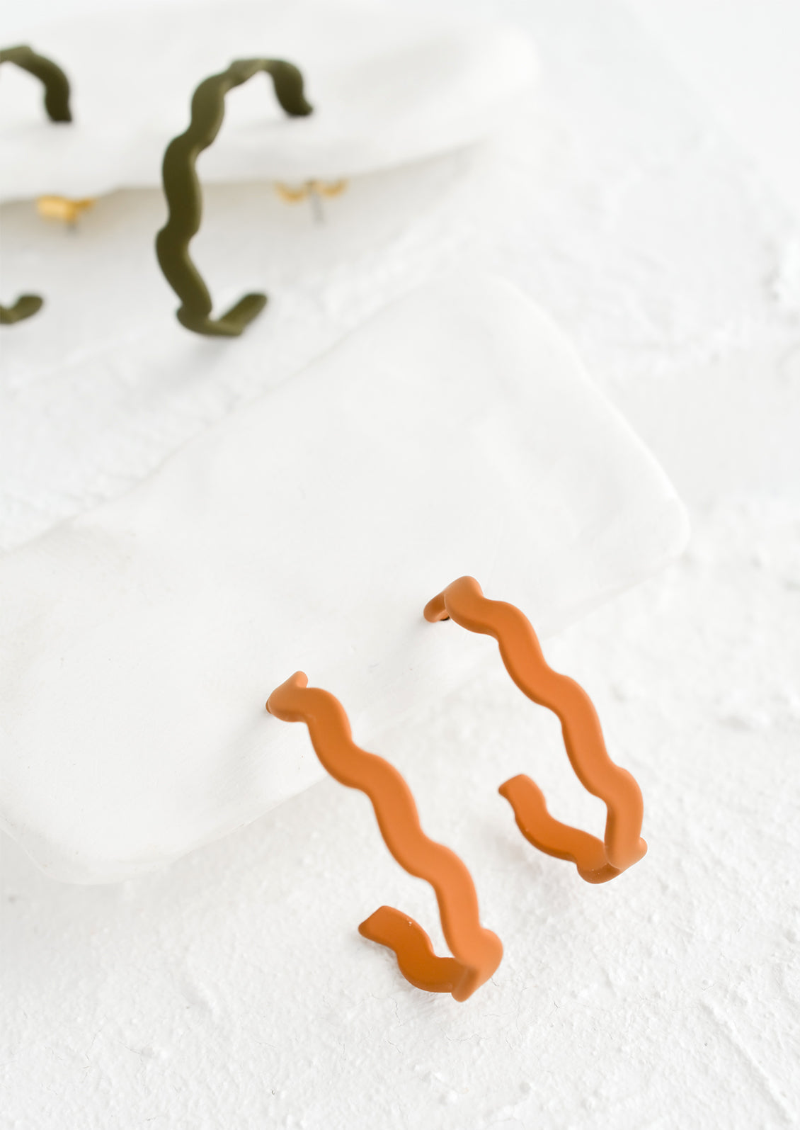 Two pairs of wavy hoop earrings in caramel and olive green.