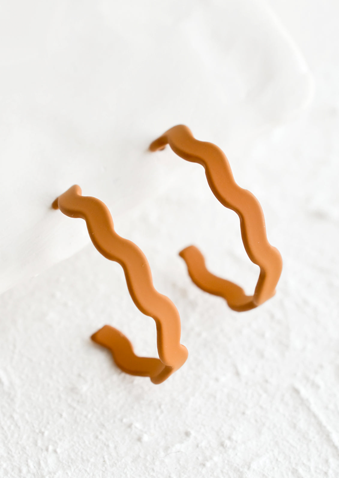 A pair of hoop earrings in matte caramel with wavy shape.