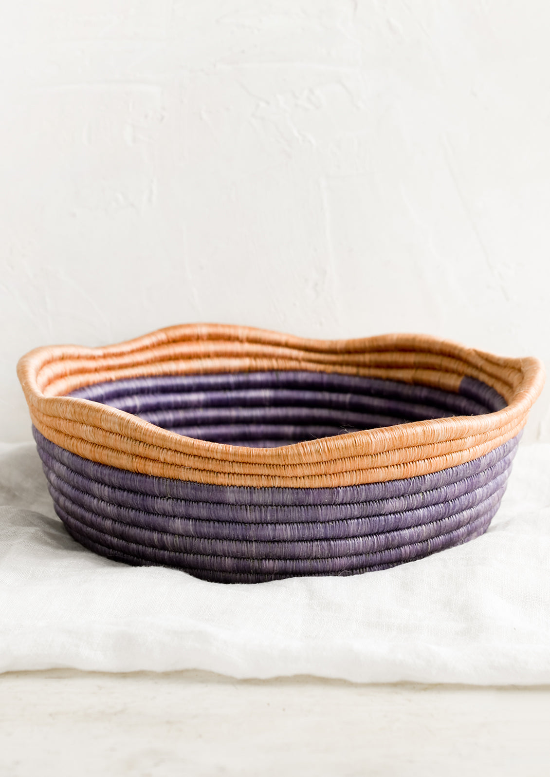 A purple woven shallow, round bowl with wavy peach rim at top.